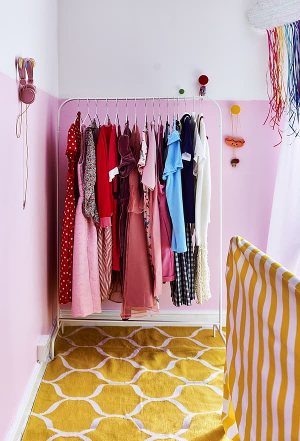 Colourful clothes hanging on a rail in a pink bedroom.