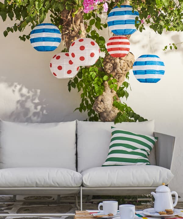 Colourful lanterns hanging from a tree above an outdoor sofa.