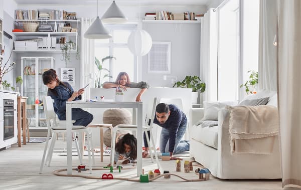 Compact-living home where a family plays with a LILLABO train set in a room with bed, sofa, table, kitchenette, and storage.