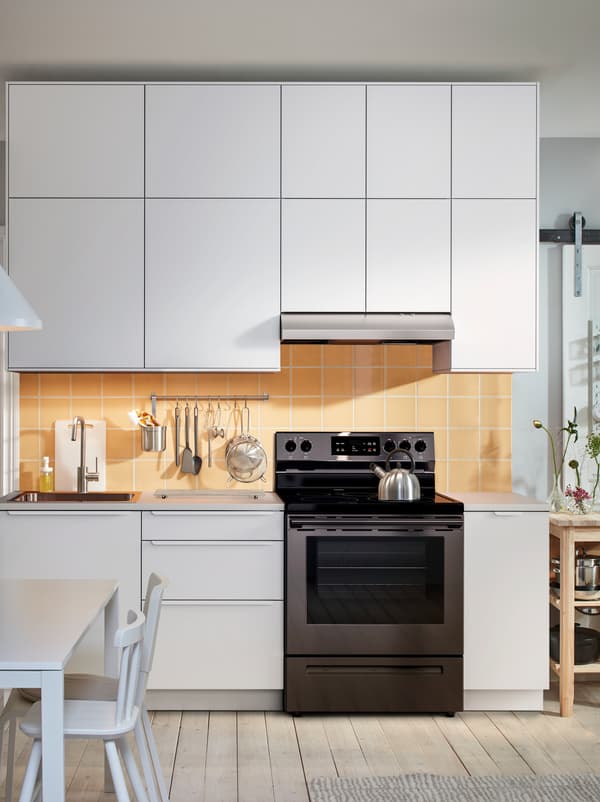 Comptoir de cuisine avec évier, table de cuisson et ustensiles au-dessus et en dessous, avec des rangées d’armoires SEKTION aux façades blanches.