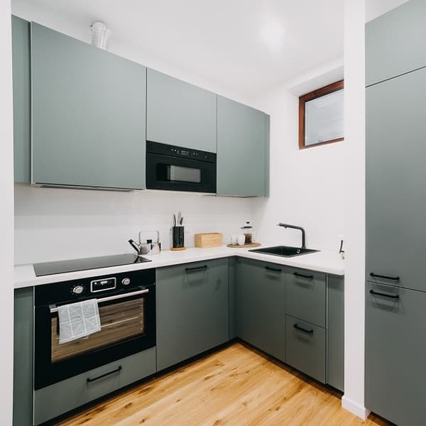 Contemporary kitchen with matte green cabinets, black fixtures, and built-in appliances.