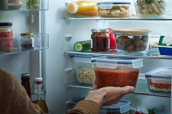 Contenedores de plástico IKEA 365+ rellenos con tallarines, salsas y verduras en el refrigerador abierto por una mano.