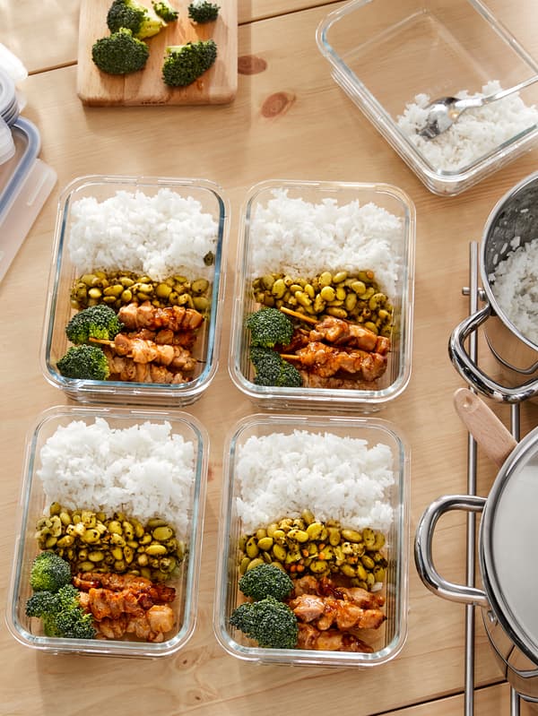 Contenitori IKEA 365+ in vetro pieni di cibo preparato in casa con strati di riso, legumi, broccoli e pollo, su un piano di lavoro