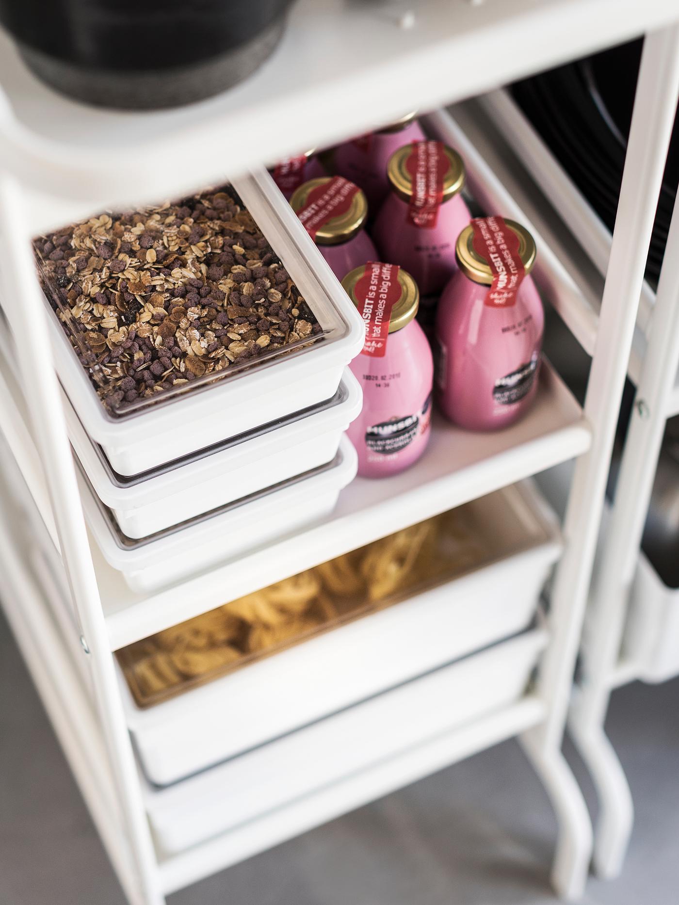 Contenitori in plastica con coperchi trasparenti contenenti muesli vicino ad alcune bottiglie rosa di smoothies, su un carrello bianco - IKEA