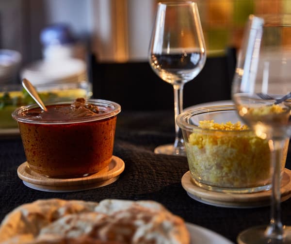Contenitori per alimenti IKEA 365+ con coperchio in bambù, riempiti con diverse pietanze, e bicchieri da vino in vetro su una tavola accogliente - IKEA