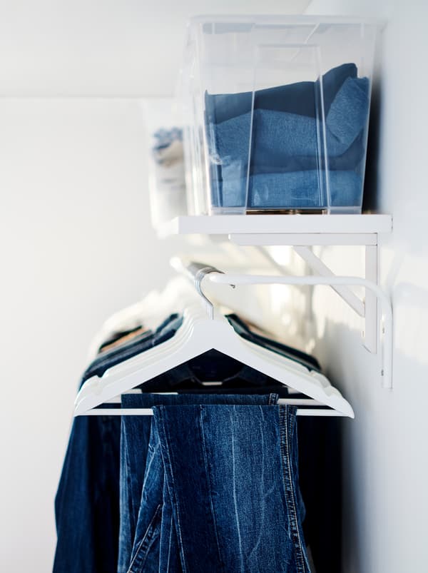 Contenitori trasparenti con indumenti ripiegati su una mensola BERGSHULT, sotto cui sono appese delle grucce BUMERANG con vestiti.
