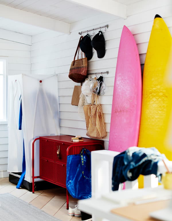 Corner of a clapboarded, white room with a VUKU wardrobe, a NIKKEBY chest of drawers and surfboards leaning against the wall.