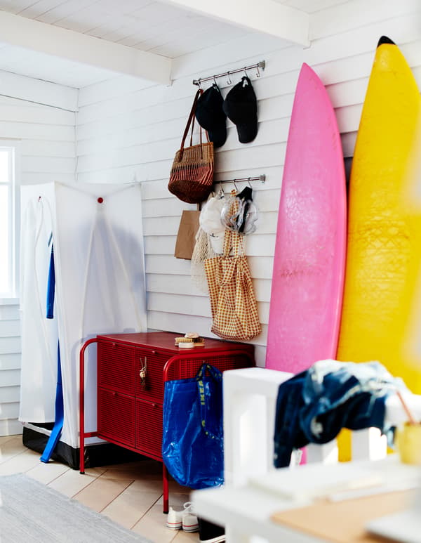 Corner of a clapboarded, white room with a VUKU wardrobe, a NIKKEBY chest of drawers and surfboards leaning against the wall.