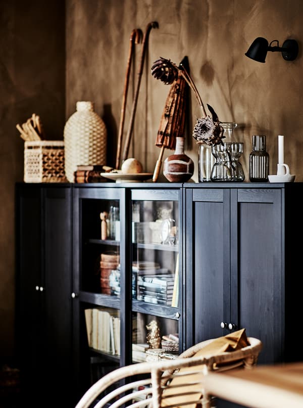 Corner of a living room with a dark, wide HAVSTA cabinet filled and covered with artful objects in natural materials.