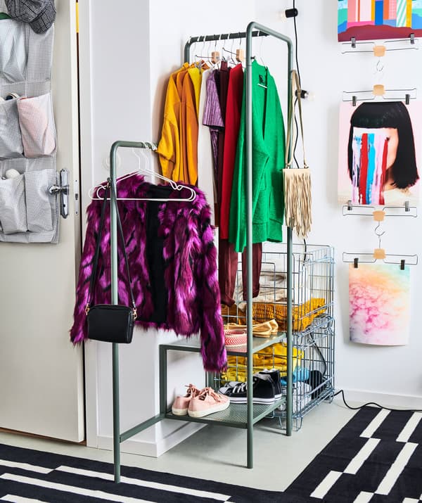Corner of a room dedicated to a small, openly stored wardrobe, hung on a clothes rack and folded in metal-wire crates.