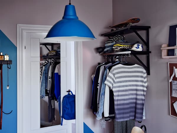 Corner of a room with a mirror on a door clothes on shelves and a rail 