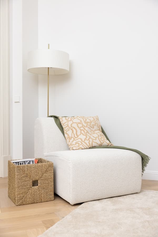 Cosy reading nook with a pouffe, floor lamp and decorative cushion.