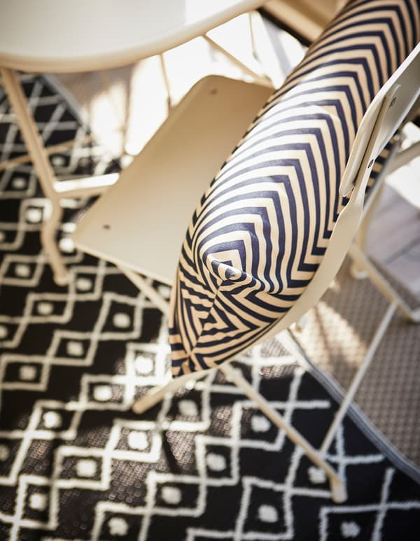 Coussin à motifs noir et blanc posé sur une chaise et tapis noir et blanc sur le sol, vus d’en haut.