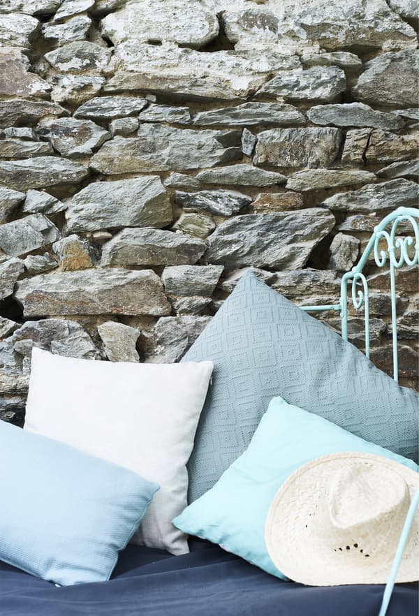 Coussins aux tons de bleus variés contre le mur de pierre