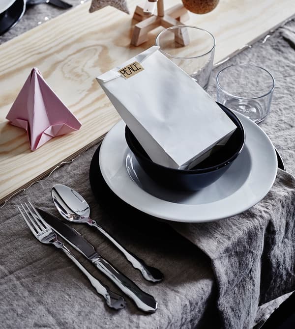 Couvert dressé avec vaisselle noire et blanche, décorations en papier et planche en bois en guise de chemin de table.