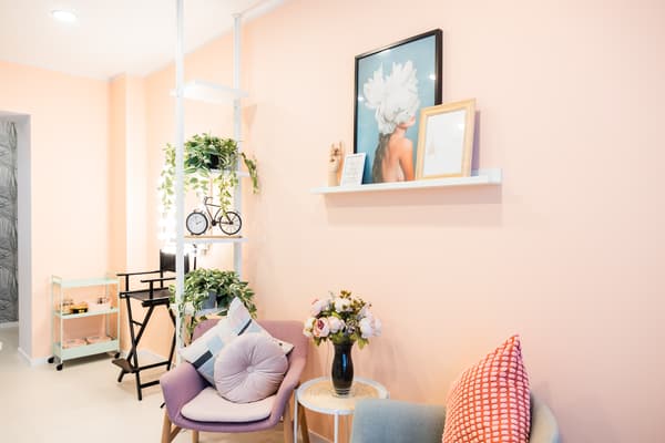 Cozy beauty salon waiting area with pink walls, stylish armchairs, and floral decor.