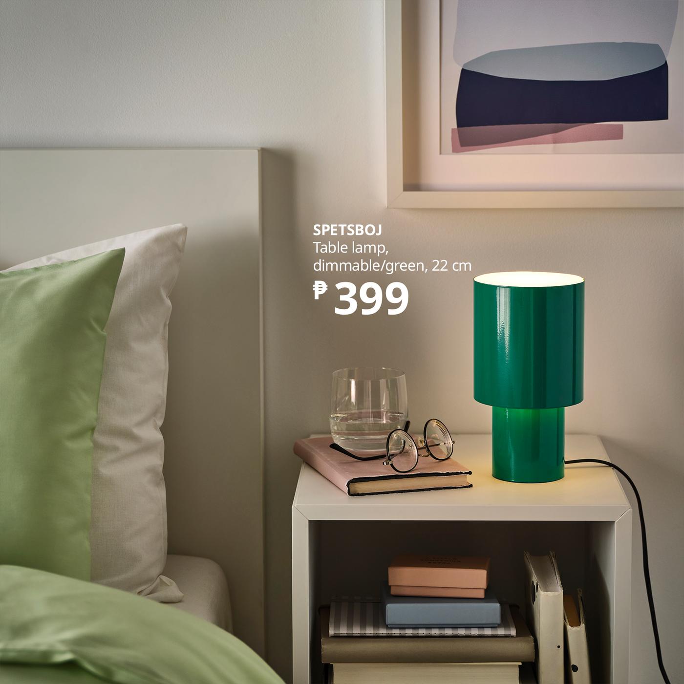 Cozy bedroom with green SPETSBOJ dimmable table lamp on bedside table, glasses and books nearby; framed art and soft lighting create a calm mood.