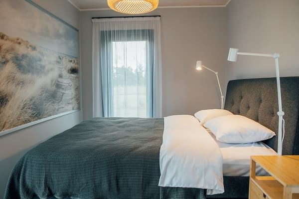 Cozy bedroom with grey upholstered bed and white reading lamp – Modern bedroom interior with dark grey headboard, soft bedding, and large window with sheer curtains.