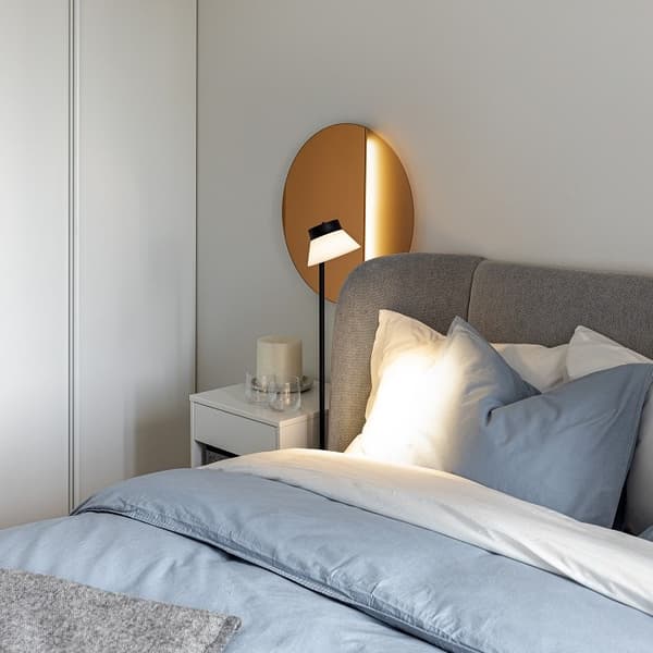 Cozy bedroom with upholstered bed, bedside table, and round decorative mirror.
