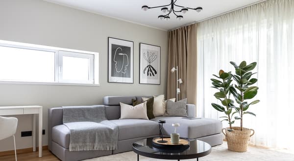 Cozy living room with grey sofa, wall art, and large windows with curtains.