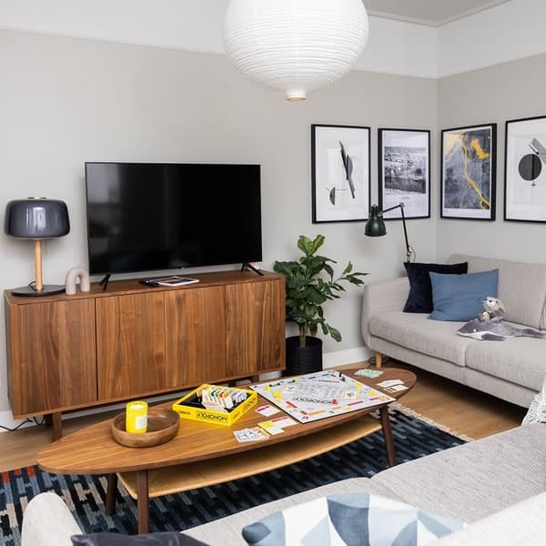 Cozy living room with grey sofas, wooden TV stand, framed wall art, and Monopoly board game on coffee table.