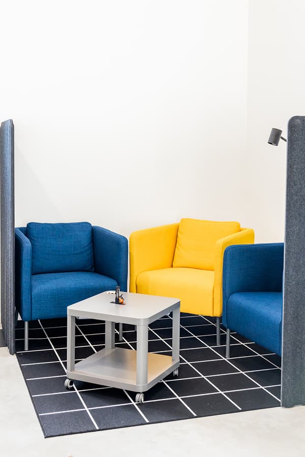 Cozy office lounge with blue and yellow armchairs around a small table on a checkered rug.