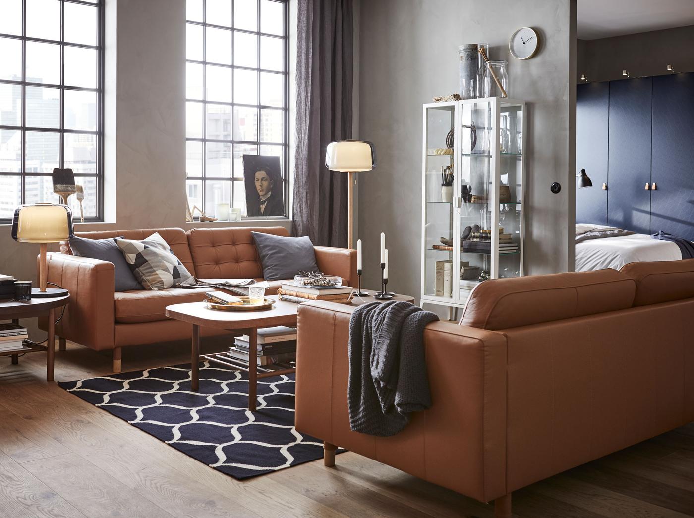 Create a modern yet airy living room space with glass MILSBO storage cabinet, sleek LANDSKRONA brown leather sofas and dark wood LISTERBY coffee tables.