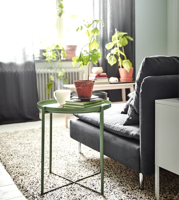 Créez un séjour contemporain en combinant des meubles modernes ! Ce coin salon cosy offre une vue apaisante sur la fenêtre. Utilisez une table/plateau pour y déposer des choses. IKEA propose beaucoup de tables/plateaux comme GLADOM, en vert foncé avec plateau amovible.