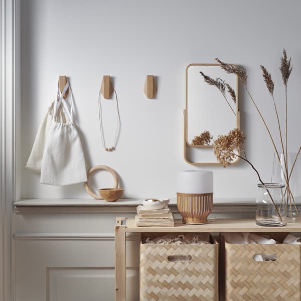 Crochets en bambou et miroir au mur, au-dessus d’un rangement en bois garni de boîtes en bambou.