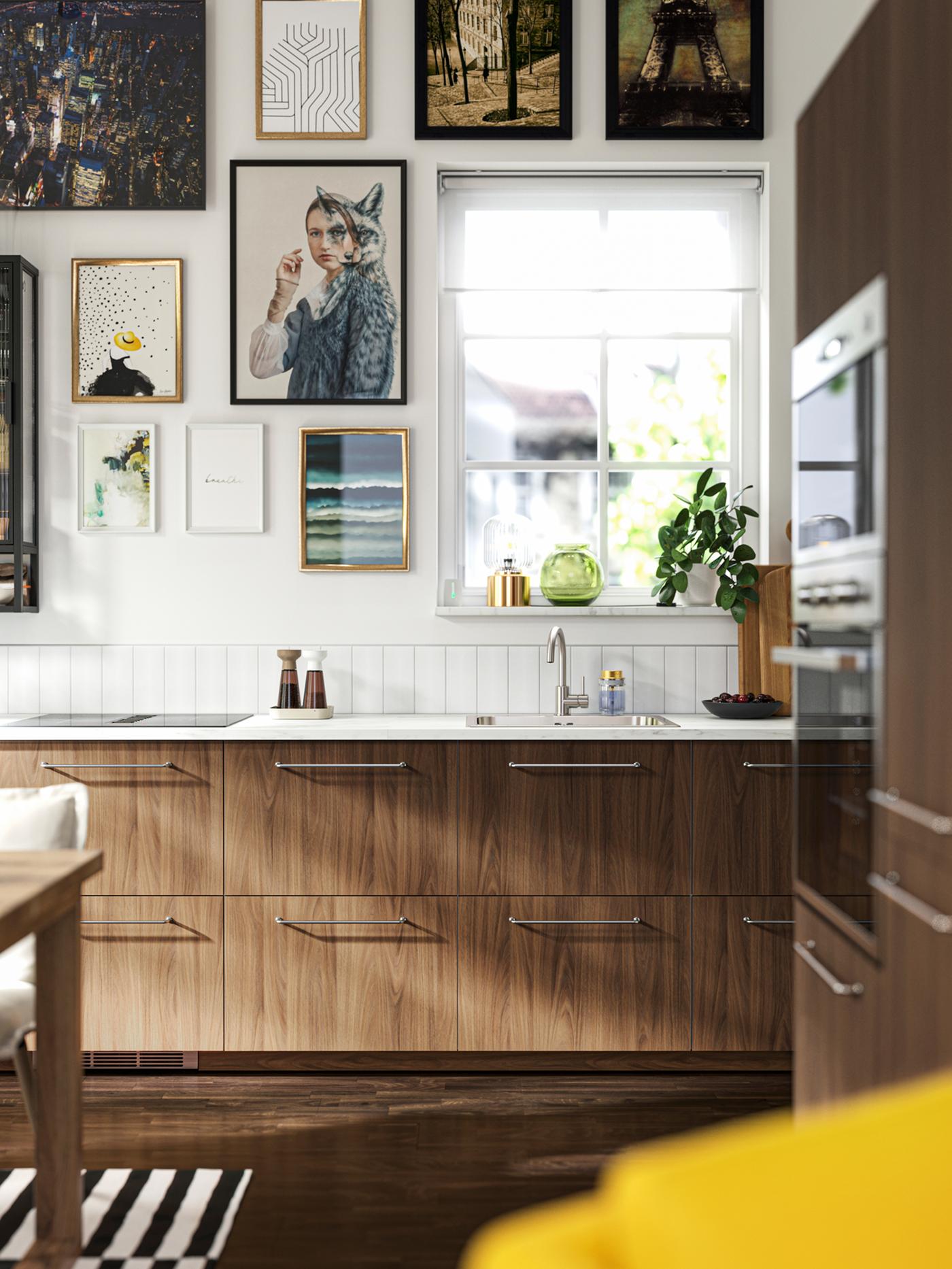 Cuisine avec façades TISTORP en motif noyer brun, sol en bois foncé et affiches sur le mur, près d’une fenêtre.
