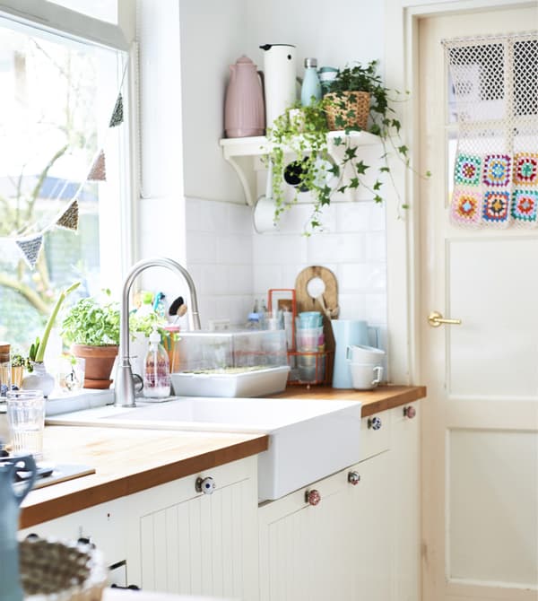 Cuisine blanche avec récipients pastel et plantes sur une tablette.