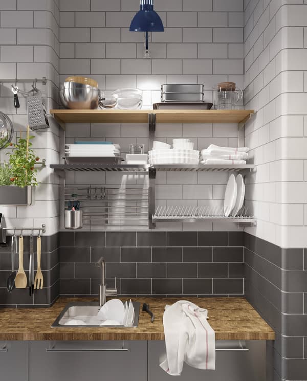 Cuisine en acier inoxydable, plan de travail en bois, lampe de travail bleue et égouttoir à vaisselle, plus rails à crochets et étagères fixés au mur.