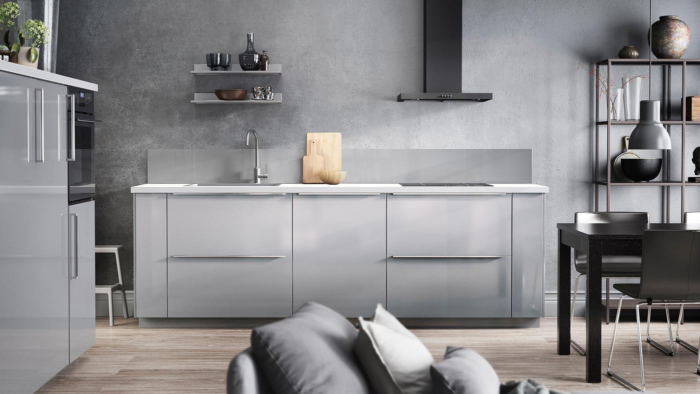 Cuisine grise avec façades de tiroirs RINGHULT brillantes et portes gris clair, plan de travail blanc et hotte noire.