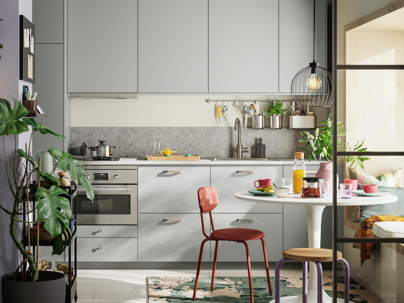 Cuisine linéaire avec façades HAVSTORP gris clair, table DOCKSTA blanche, chaise ÖSTANÖ brun-rouge et tabouret DOMSTEN.