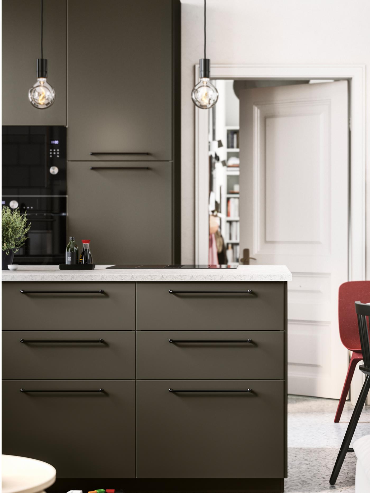Cuisine ouverte avec façades HAVSTORP brun-beige, poignées et électroménagers noirs, et plan de travail effet calcaire.
