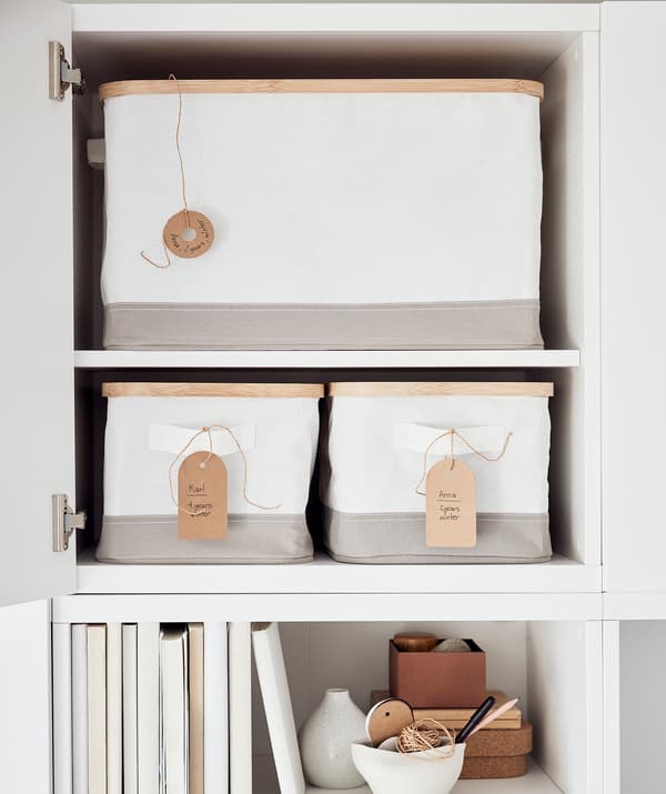 Cupboard with door open, revealing RABBLA storage boxes with handwritten tags. Below the cupboard is a shelf with books.