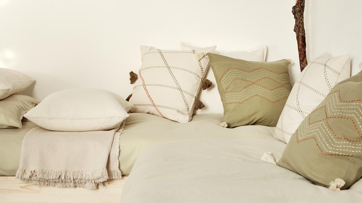 Cushions in different covers, including off-white HERVOR cushion covers and green HALLVI cushion covers, sit on beds.