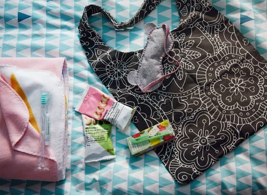 Dans un sac VÄNSKAPLIG noir, déposez quelques collations, boîtes à boire et un loup. Quel joli petit cadeau de bienvenue pour l'amie qui dort à la maison&thinsp;! Le sac à motif floral est assez grand pour contenir une couverture.