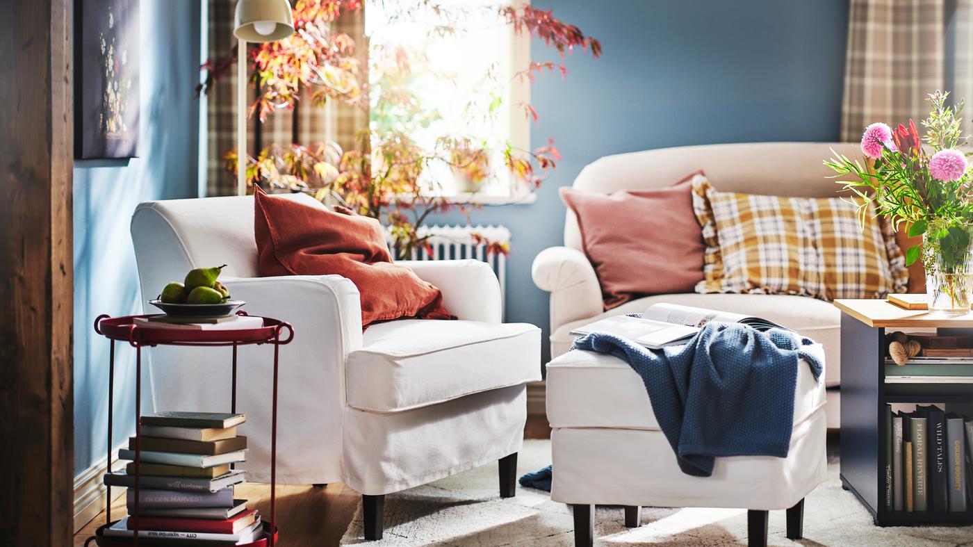 Dans un séjour lumineux, un fauteuil ROCKSJÖN blanc et un repose-pieds ROCKSJÖN blanc à côté d’un canapé ESSEBODA beige clair.