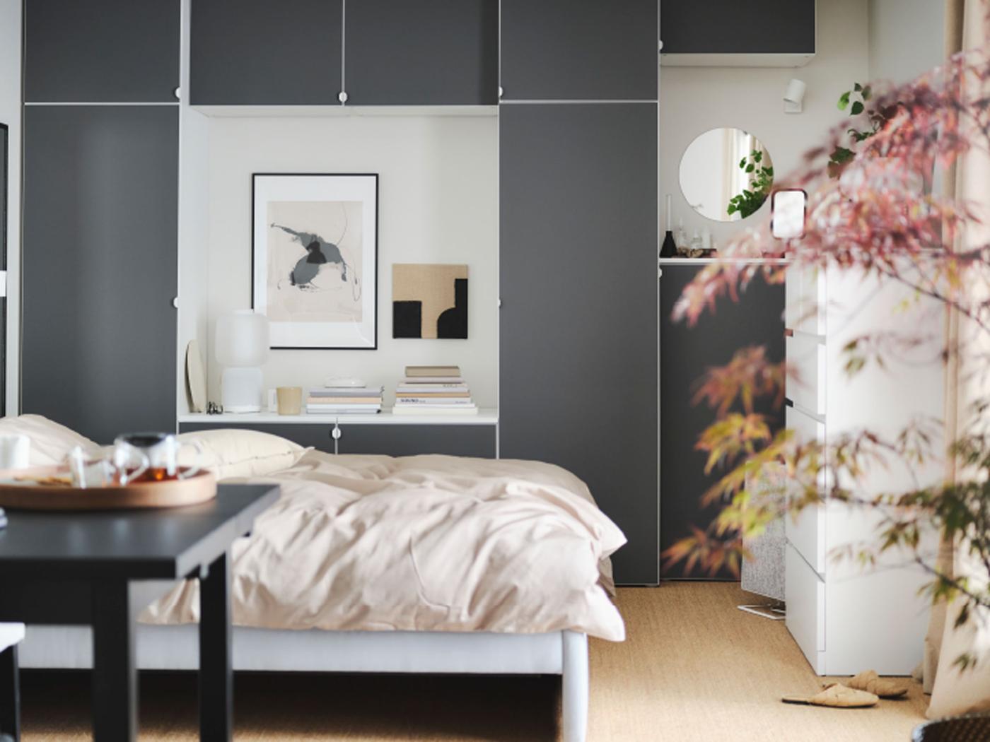 Dans une chambre paisible, un lit GLADSTAD gris, un bureau en bois, une armoire-penderie grise aux volumes dynamiques et des lampes rondes suspendues au plafond.