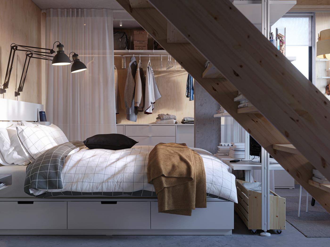 Dans une petite chambre à coucher de style minimaliste, lit NORDLI avec rangement, tête de lit et dressing isolé par des rideaux.