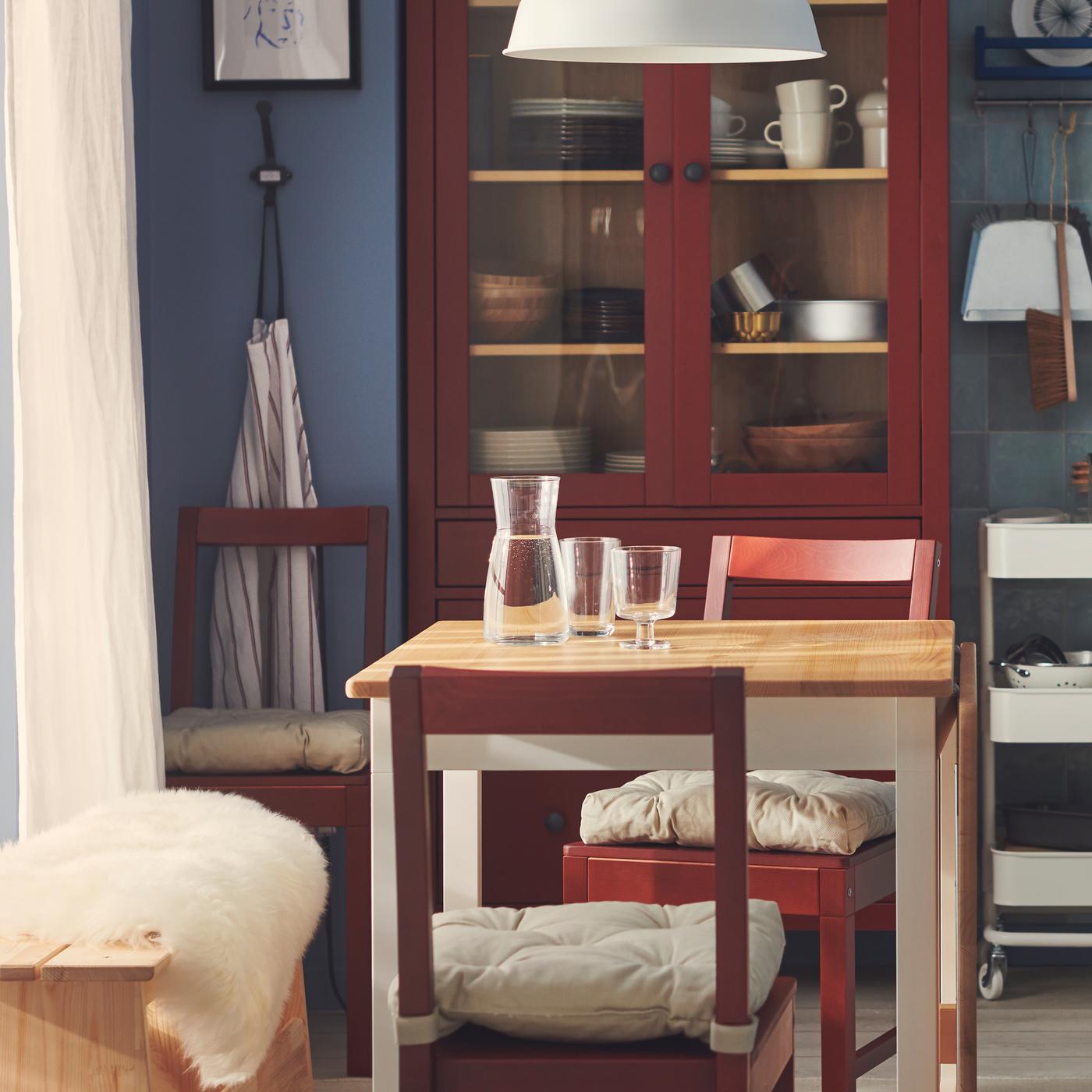Dans une salle à manger de style maison de vacances suédoise aux murs carrelés de bleu sont installées une table et des chaises PINNTORP.