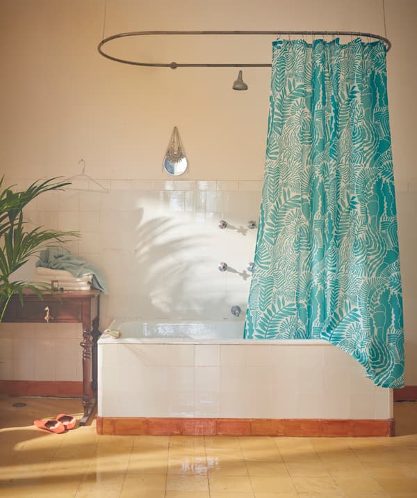 Dans une salle de bain, une baignoire avec un rideau de douche GATKAMOMILL accroché à une tringle ovale.