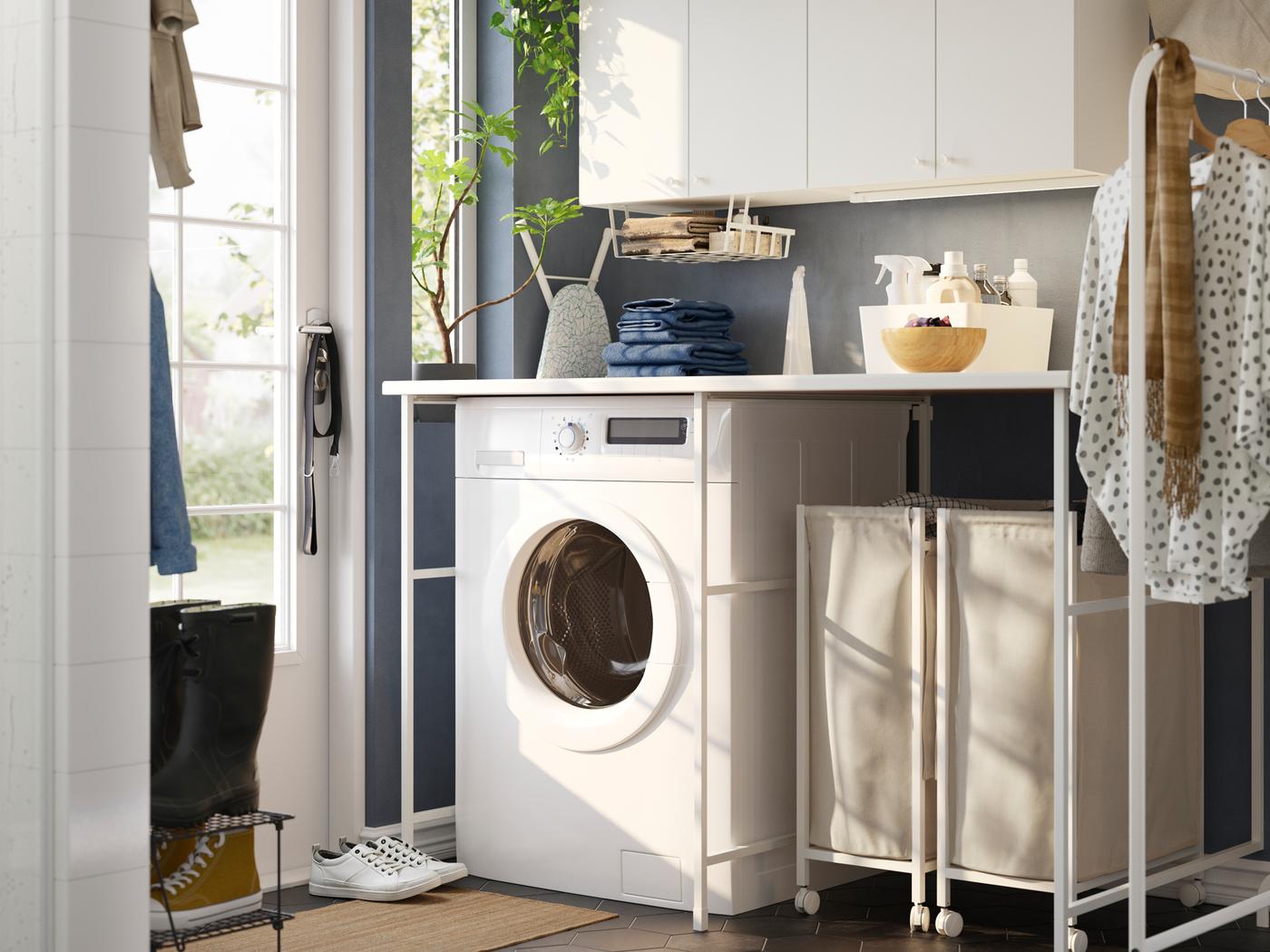 Dans une salle de lavage bleue se trouvent un rangement ENHET blanc, une laveuse, un portant et des paniers à lessive sur roulettes.