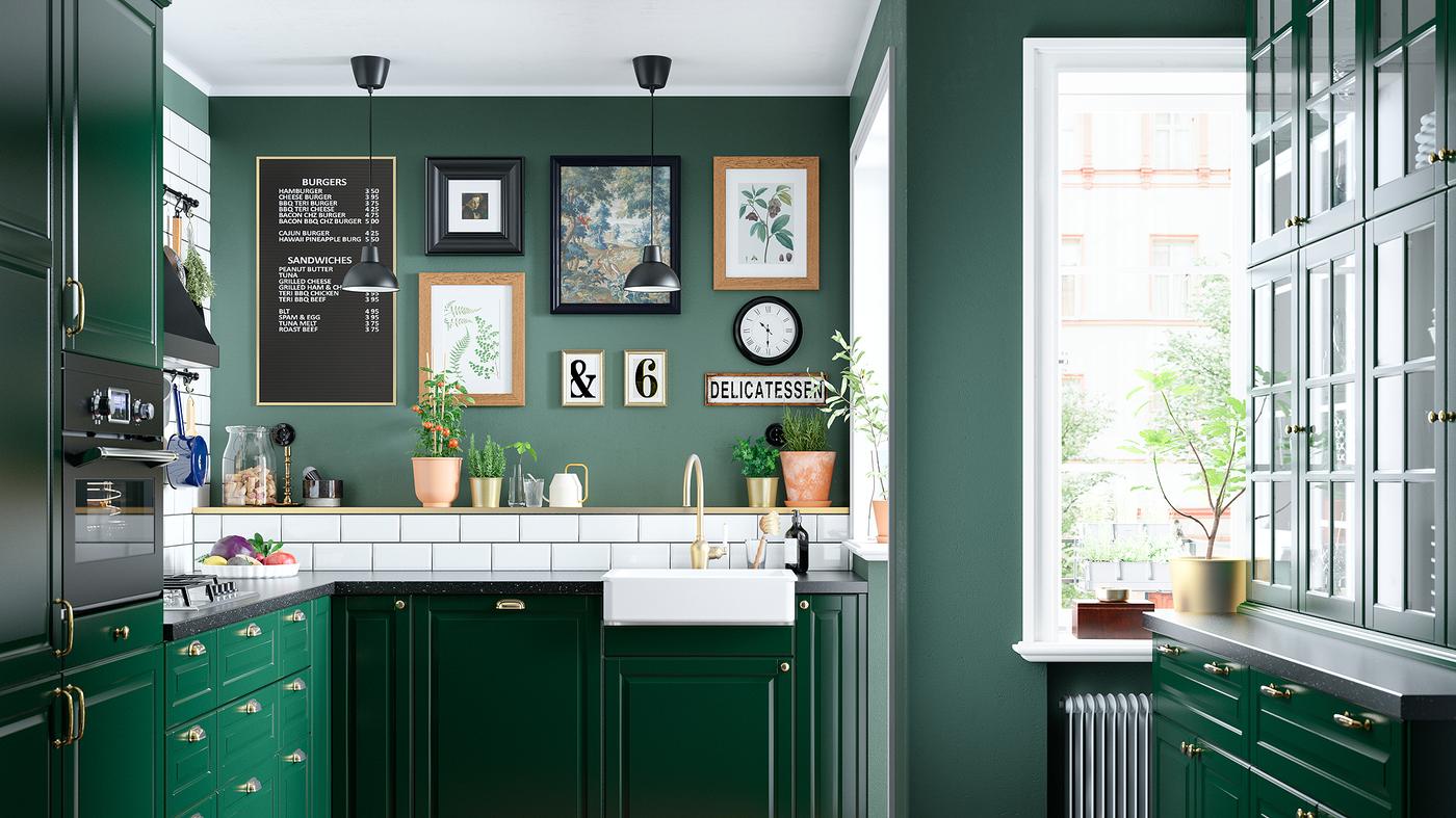 Dapur berwarna hijau dengan sink berwarna putih yang mempunyai bahagian hadapan yang boleh dilihat, paip berwarna loyang, hob gas dan dua lampu siling berwarna hitam.