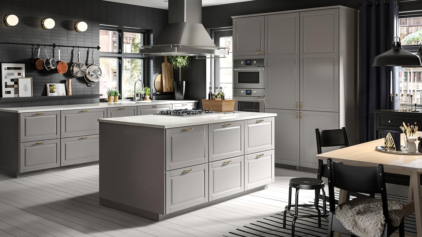 Dapur berwarna kelabu yang besar dengan pulau dapur di tengah-tengah dan meja makan kayu bic/berwarna putih dengan kerusi dan bangku berwarna hitam.