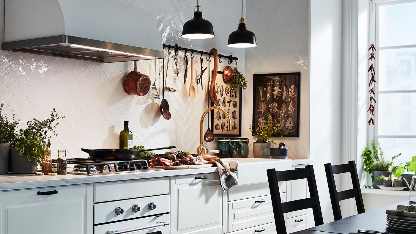 Dapur berwarna putih pudar dengan pintu dan bahagian hadapan laci BODBYN yang tradisional diterangi oleh dua lampu pendan berwarna hitam.