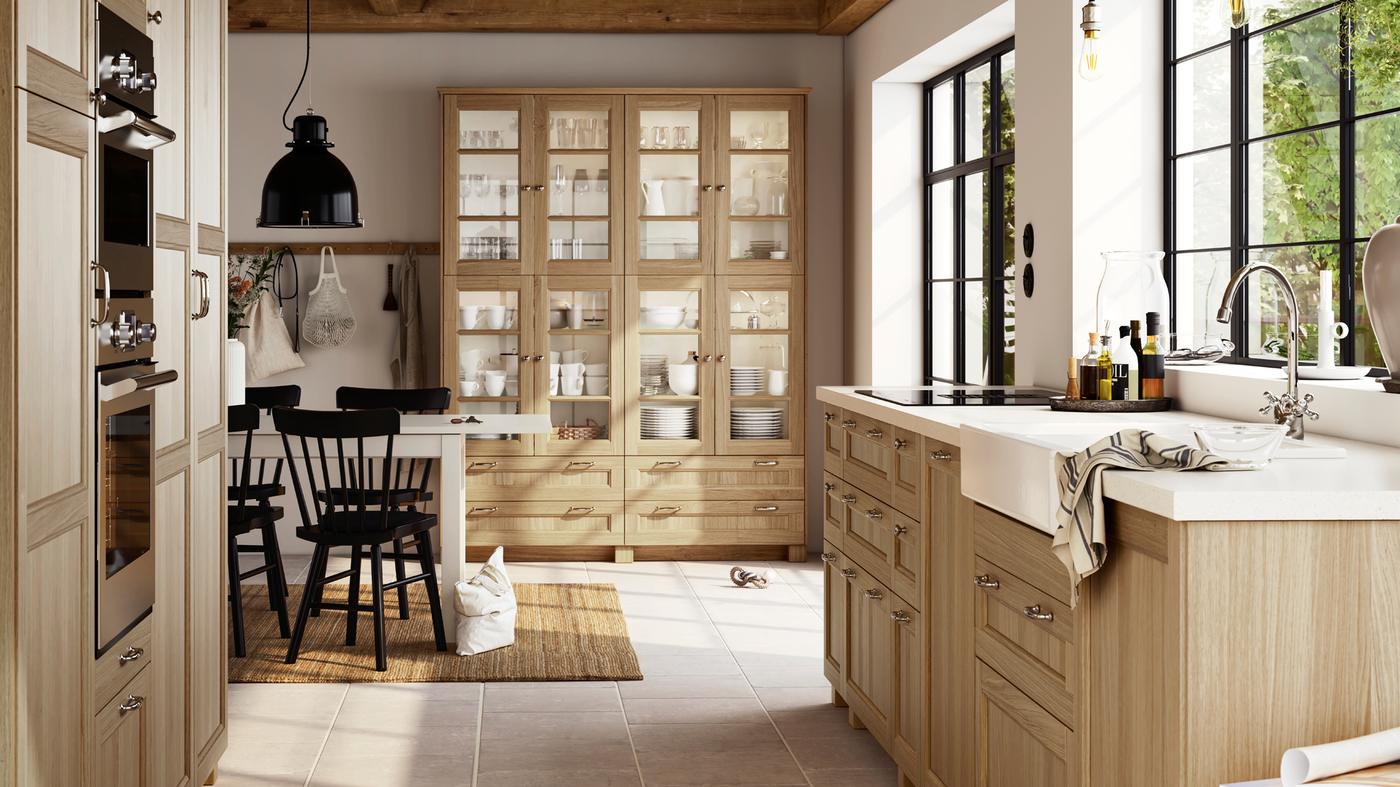 Dapur besar yang terang yang mempunyai bahagian depan VEDHAMN kayu oak, termasuk kabinet berpintu kaca yang penuh dengan barang-barang kaca dan set makan malam.
