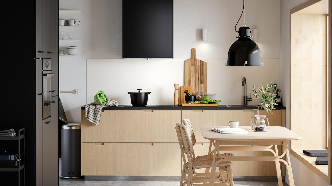 Dapur minimalis dengan bahagian hadapan laci buluh berwarna cerah, pintu berwarna hitam, meja makan buluh berwarna cerah dan dua kerusi.