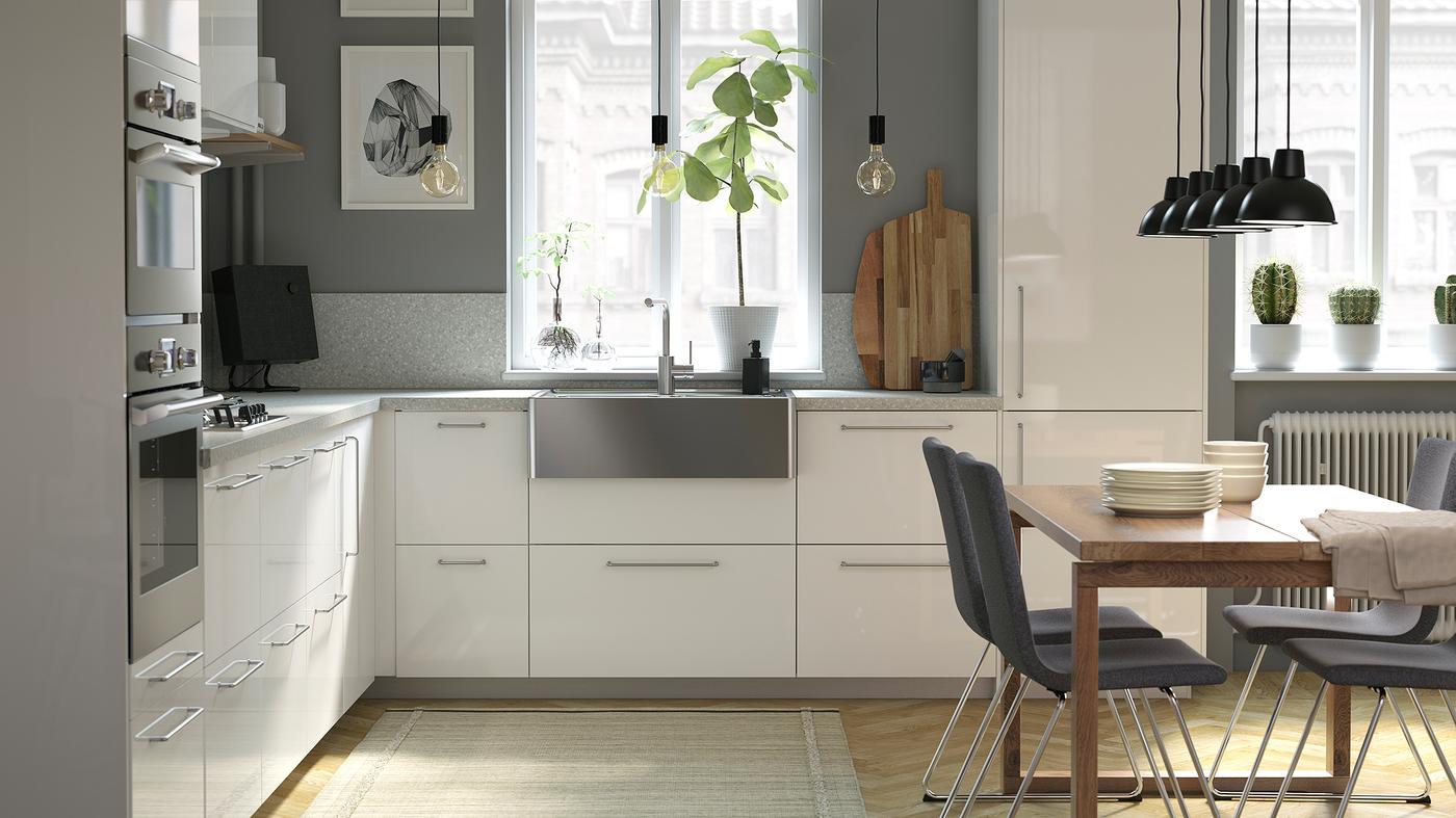 Dapur yang disinari cahaya dengan bahagian hadapan laci berwarna putih berkilat, dinding berwarna kelabu, meja kayu dan sink keluli tahan karat.